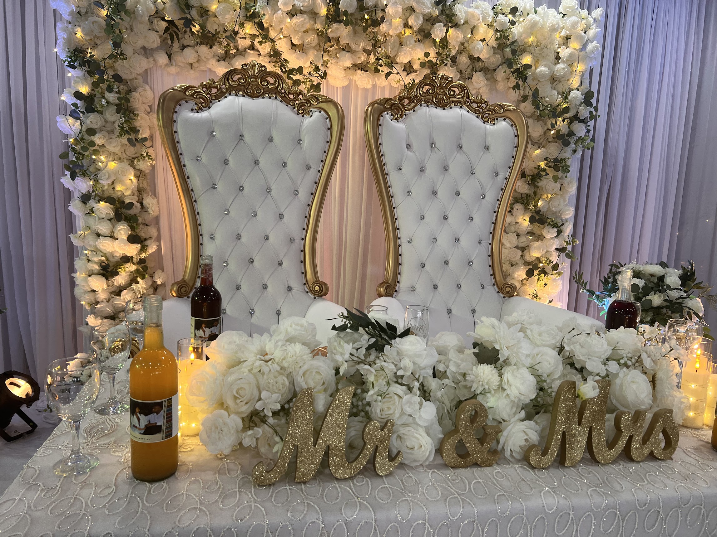 White and gold tufted throne chairs behind a floral sweetheart table with Mr & Mrs letters